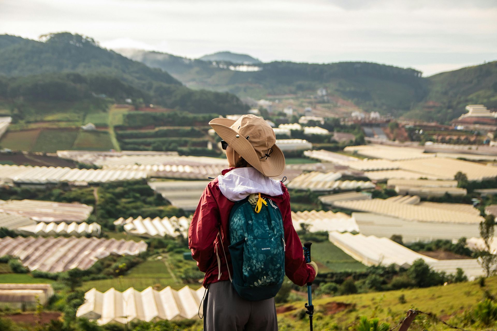 A lone mountaineer carrying gear stands at a summit, gazing down at the expansive valleys and rugged mountain peaks.