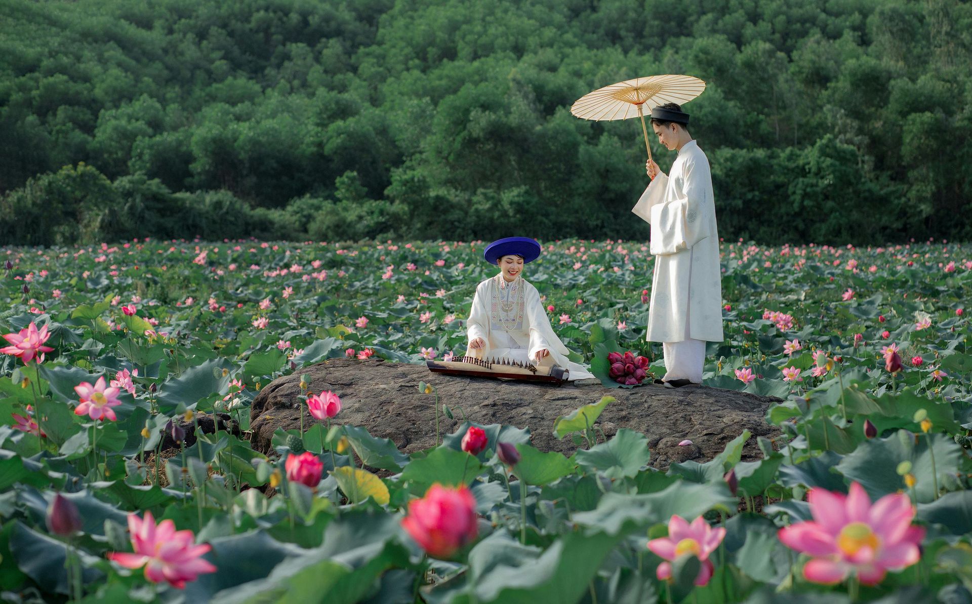 Two women in traditional Vietnamese attire standing in a serene lotus pond, surrounded by vibrant pink lotus flowers.