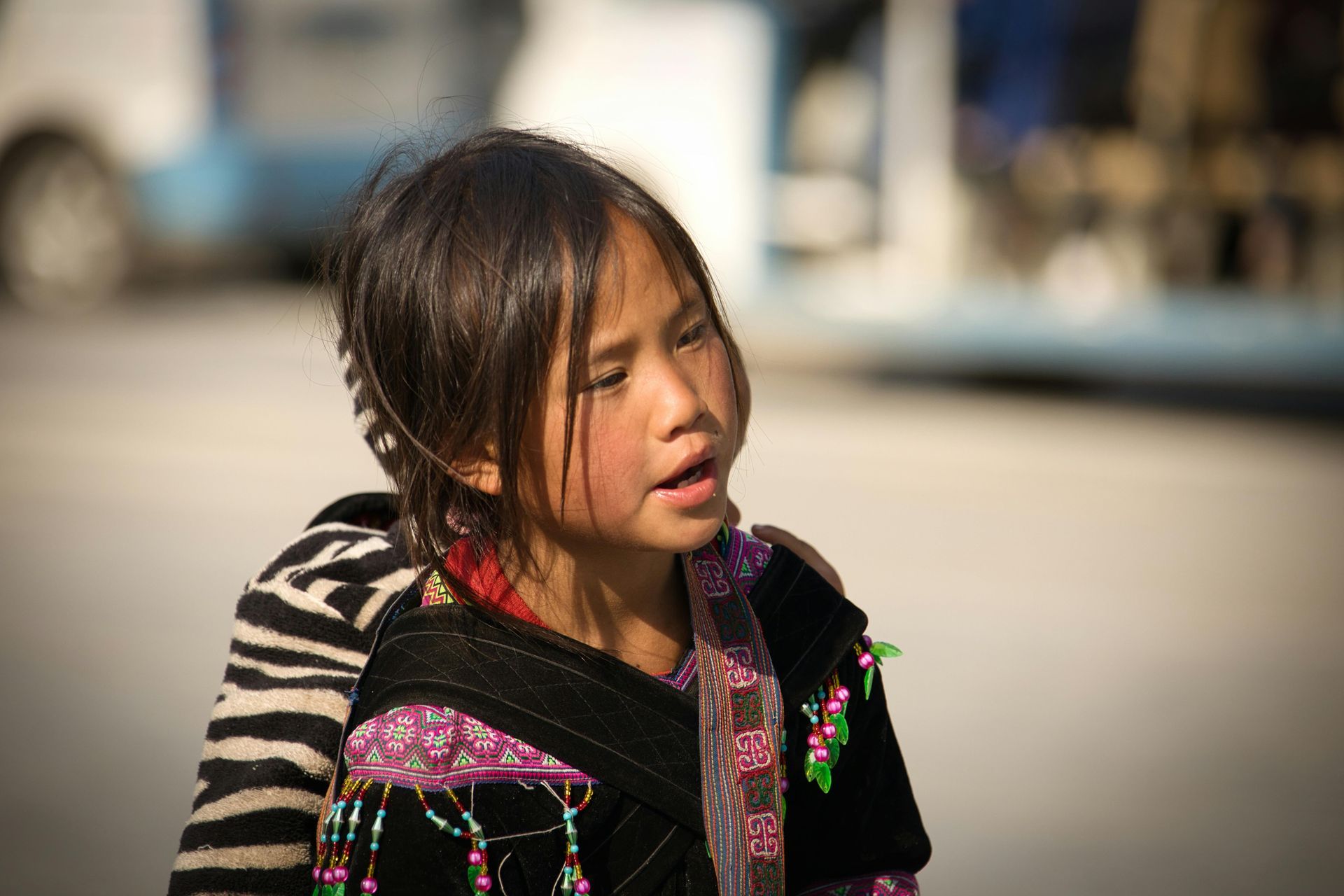 A young ethnic minority girl in Sa Pa wearing traditional attire, smiling shyly against the backdrop of terraced fields.