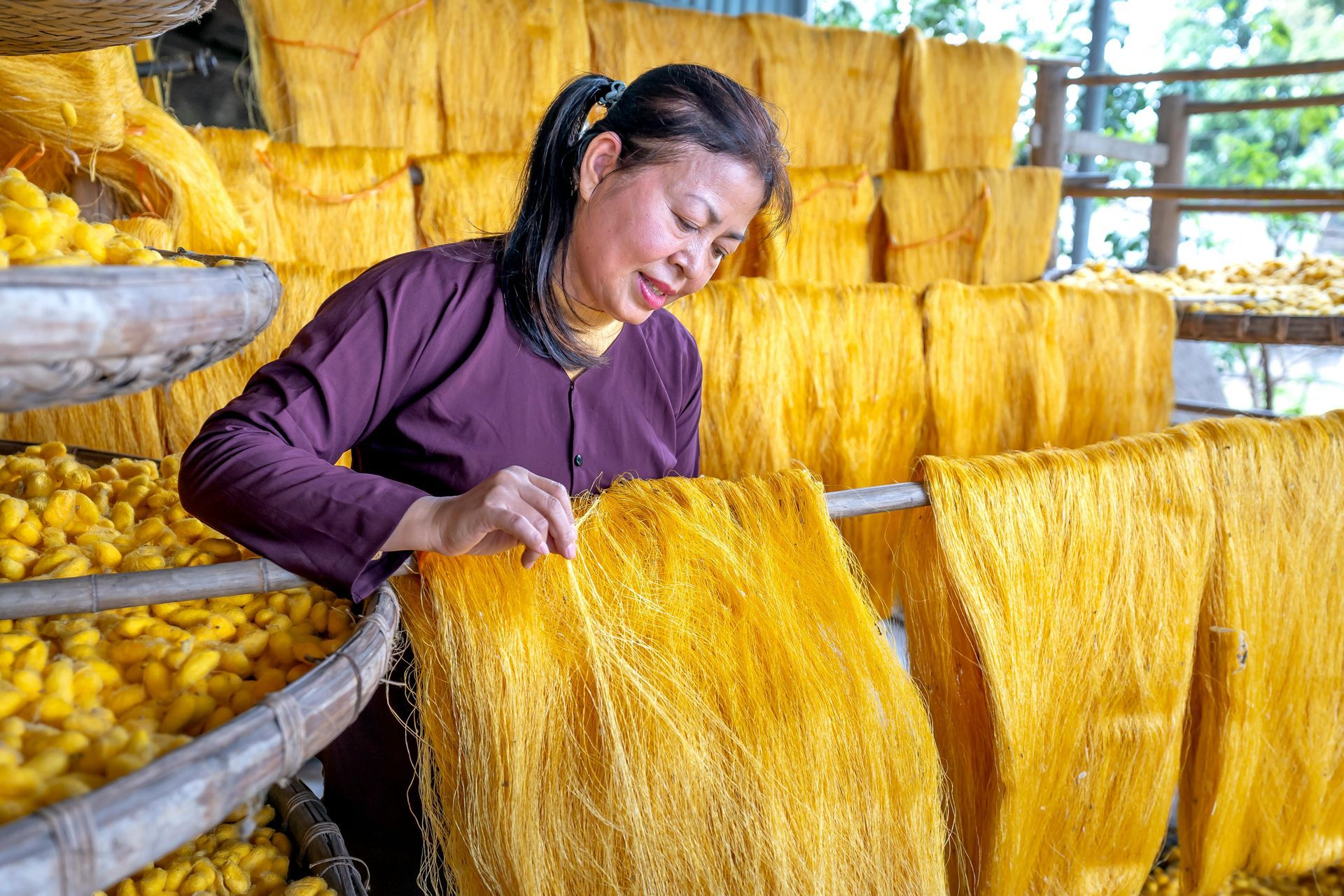 A silk-weaving artisan operating a loom to produce delicate silk threads, with rolls of silk stretching across the workspace.