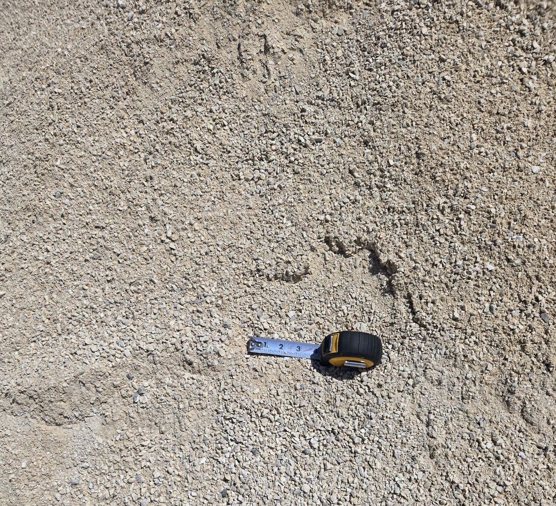 A tape measure is laying on top of a pile of gravel.