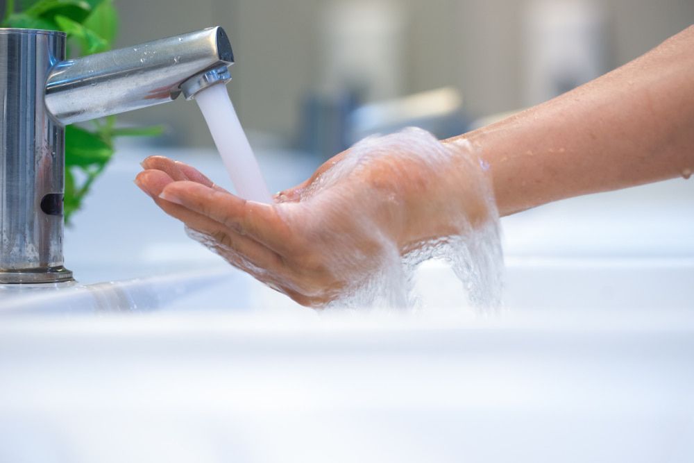 A Person Is Washing Their Hands in A Bathroom Sink — Custys Plumbing Services in Trinity Park, QLD