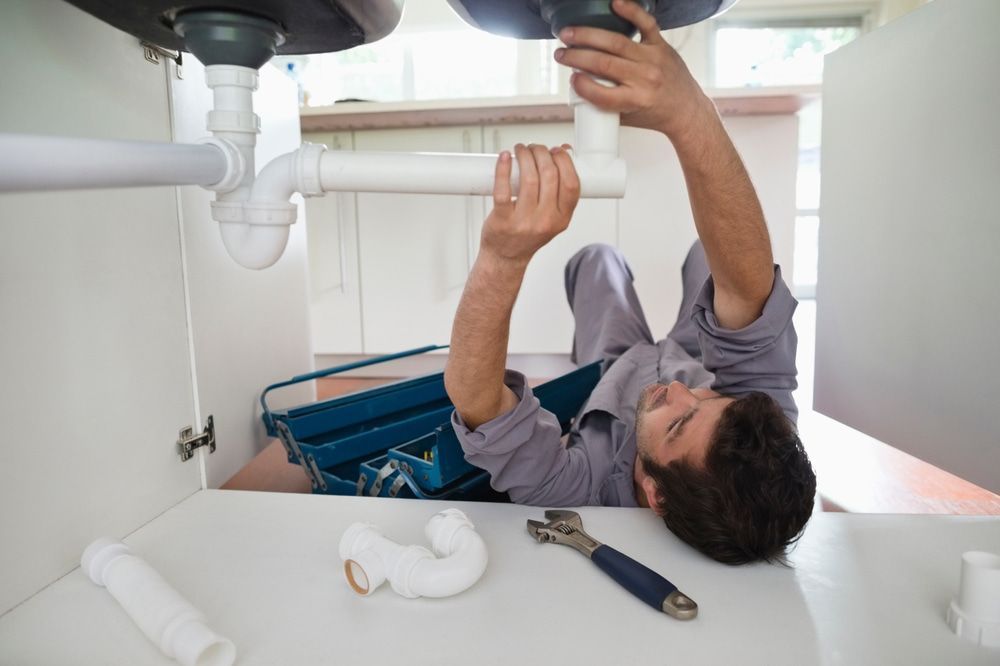 A Plumber Is Fixing a Sink Pipe in A Kitchen — Custys Plumbing Services in Palm Cove, QLD