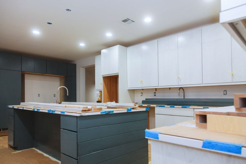 A Kitchen Under Construction with White Cabinets and A Large Island — Custys Plumbing Services in Trinity Park, QLD