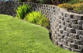 A stone wall surrounds a lush green lawn in a park built by Riverside CA retaining wall contractors