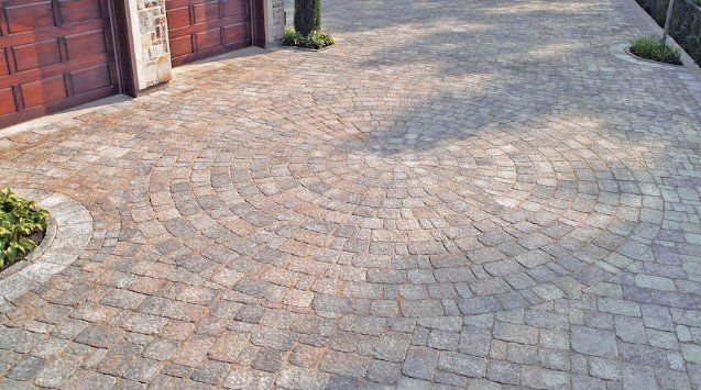 A brick driveway leading to a garage with a tree in the middle.