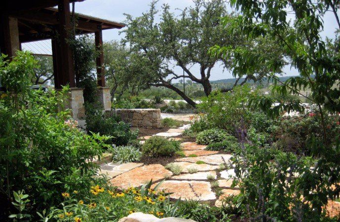 A stone walkway leading to a house surrounded by trees and flowers.