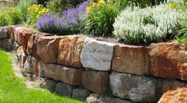 A stone retaining wall in Riverside CA is surrounded by flowers and grass in a garden.