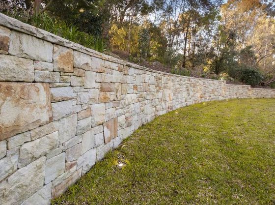 A large stone retaining wall surrounds a lush green field in Riverside California