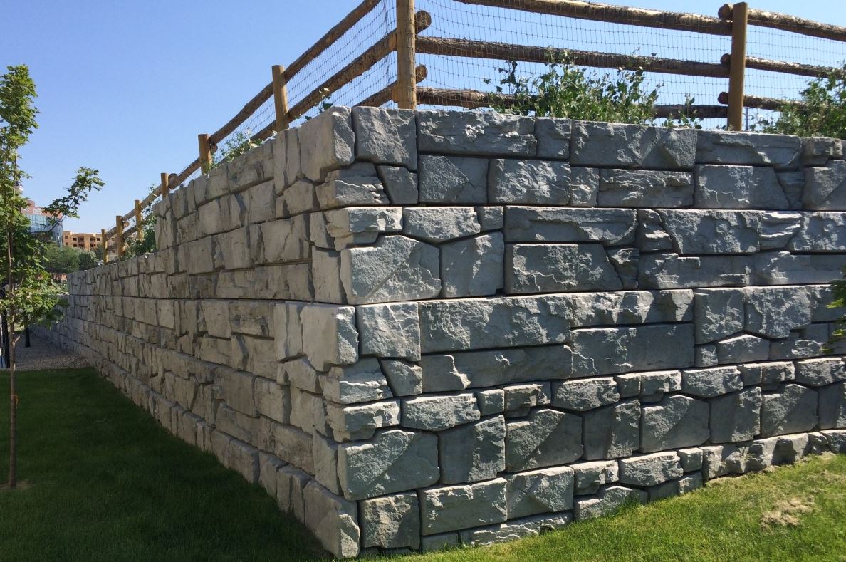 A large stone retaining wall built by Riverside retaining wall contractors with a wooden fence behind it.