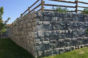 A large stone retaining wall built by Riverside retaining wall contractors with a wooden fence behind it.