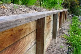 A wooden retaining wall is surrounded by plants and dirt in Riverside CA