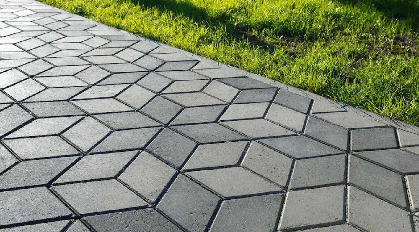 A brick walkway with a geometric pattern is surrounded by grass.