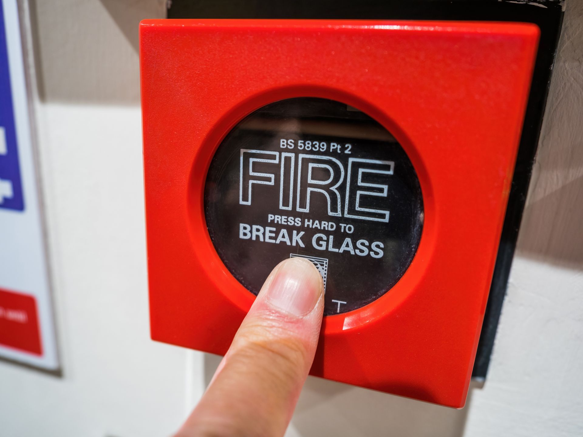 Red fire alarm call point with a finger pressing the glass labeled FIRE and BREAK GLASS