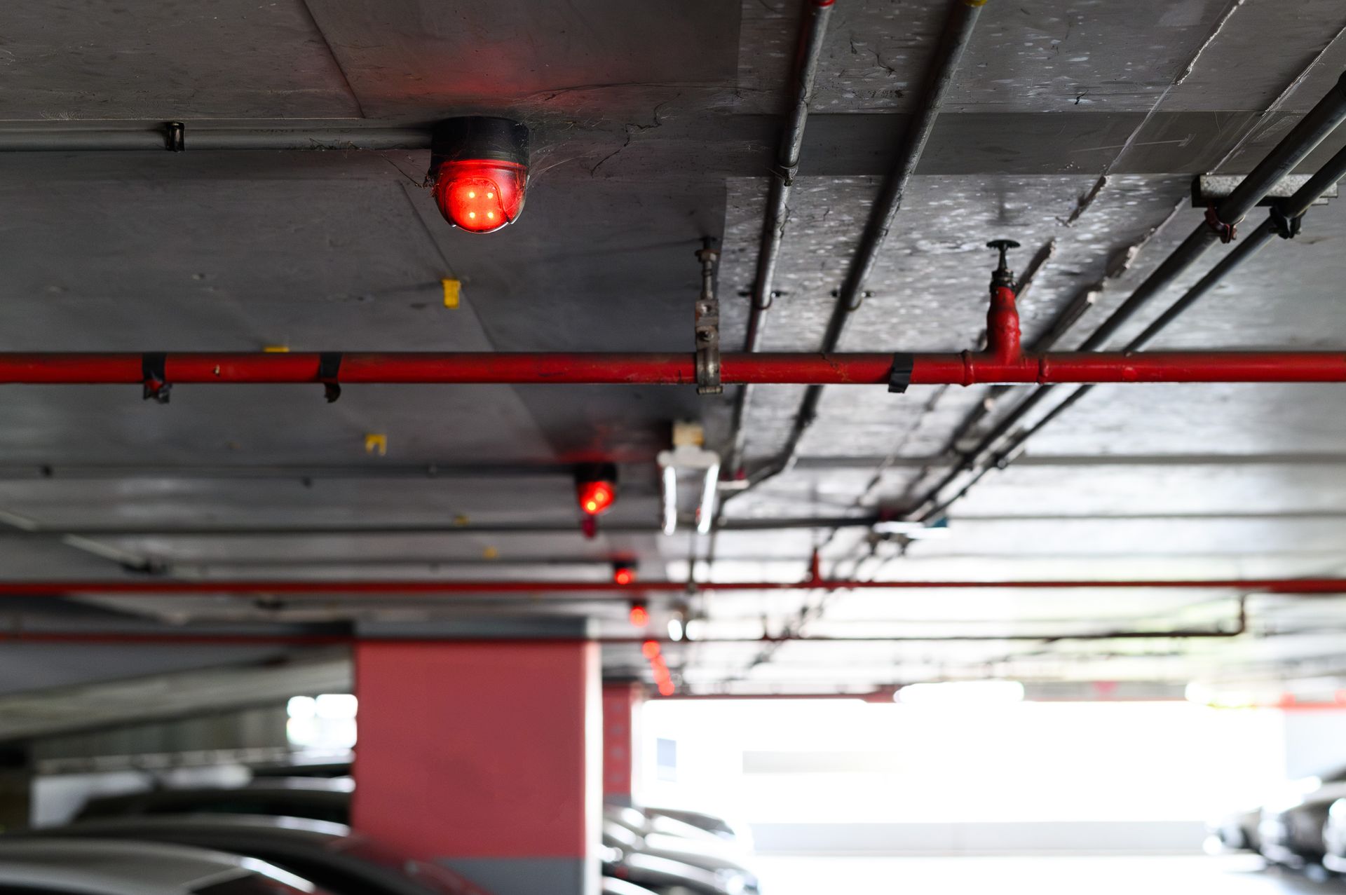 Ceiling of a parking garage with red pipes and warning lights, seen from below