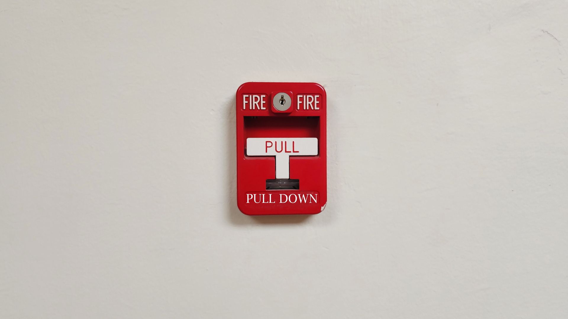 Red fire alarm pull station mounted on a white wall.