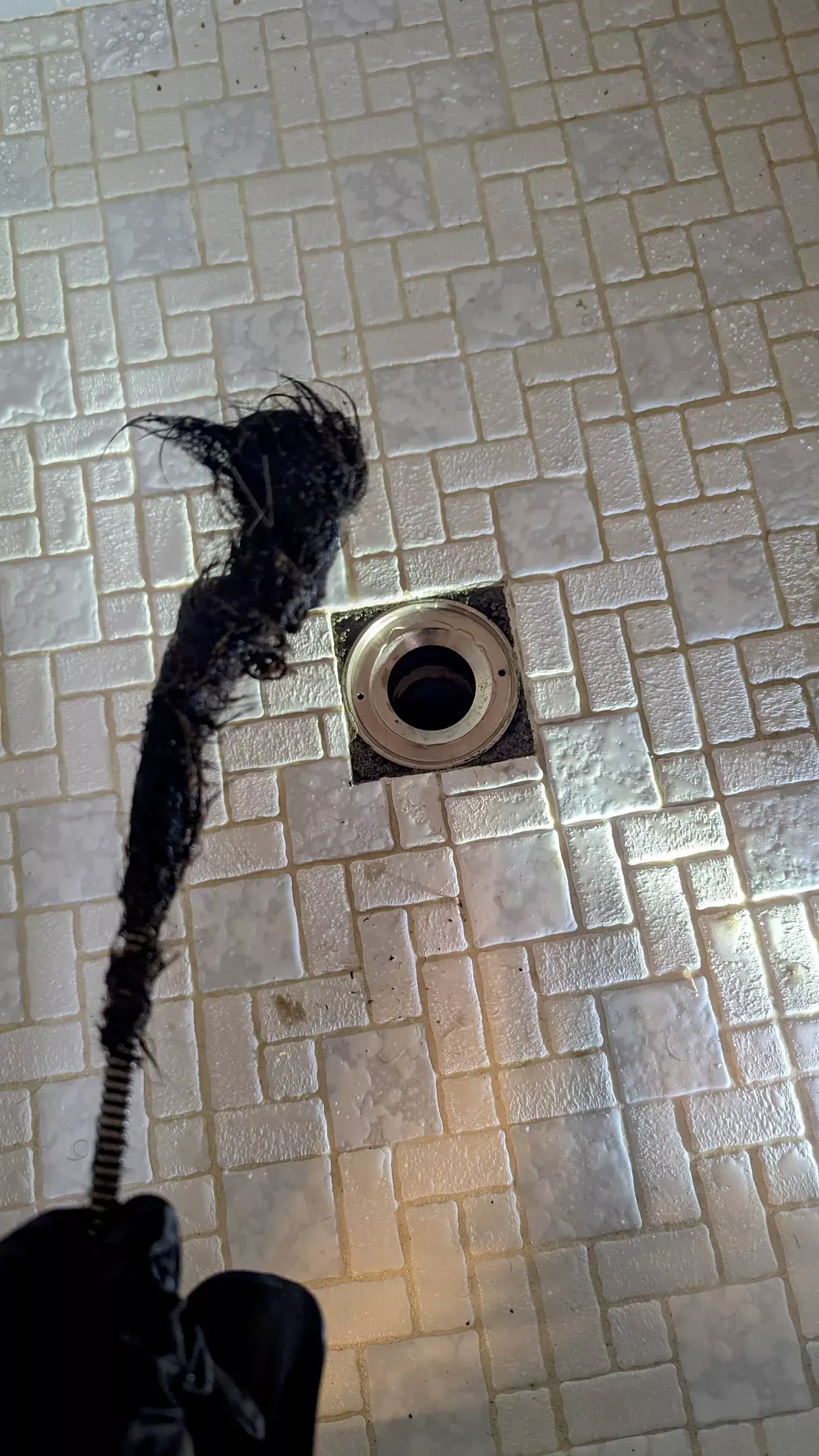 A drain snake with a large clump of hair pulled from a shower drain. Gray tile floor.