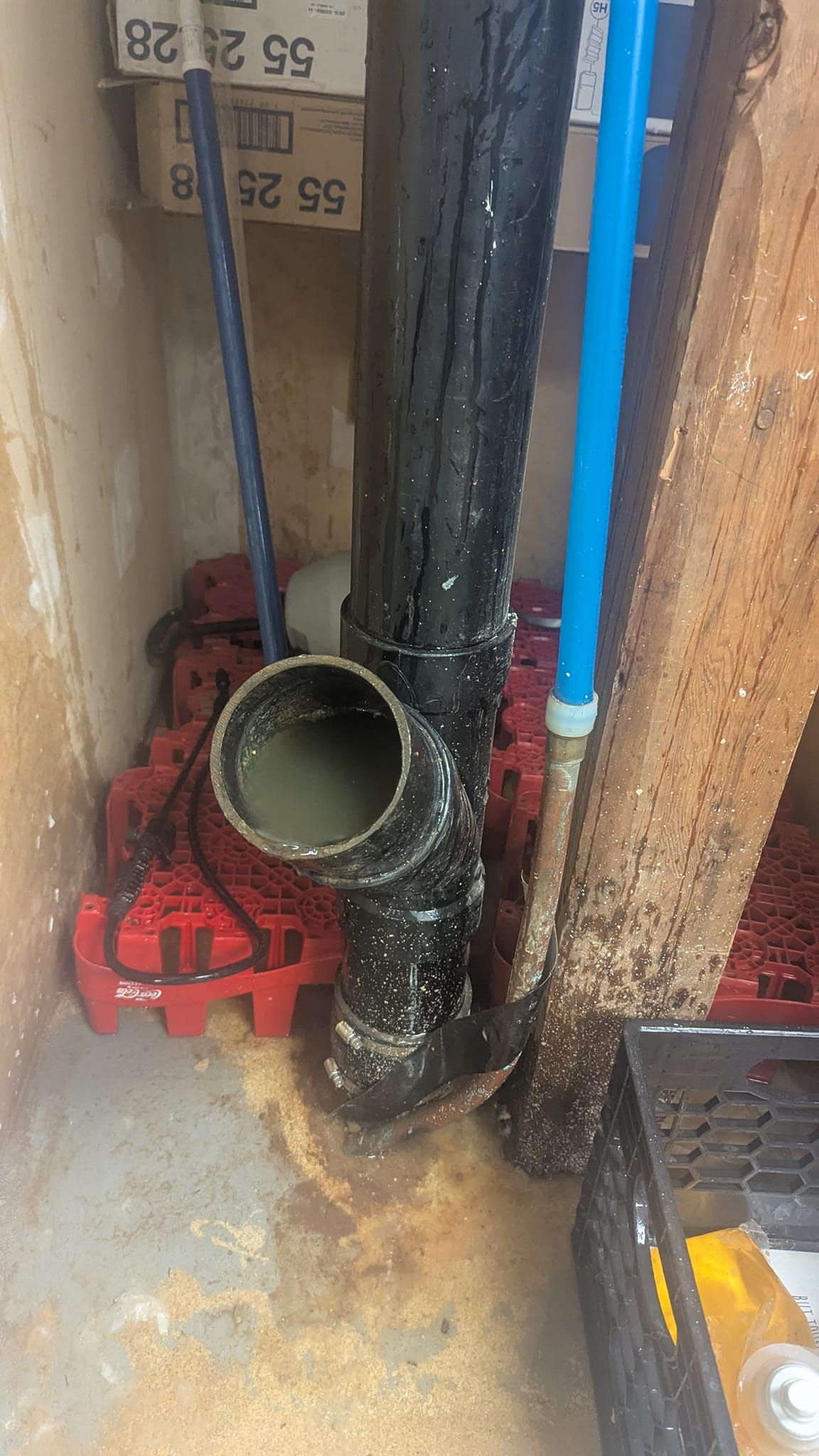 Black drain pipe with a water puddle at the opening, set on red plastic grates in an alcove.