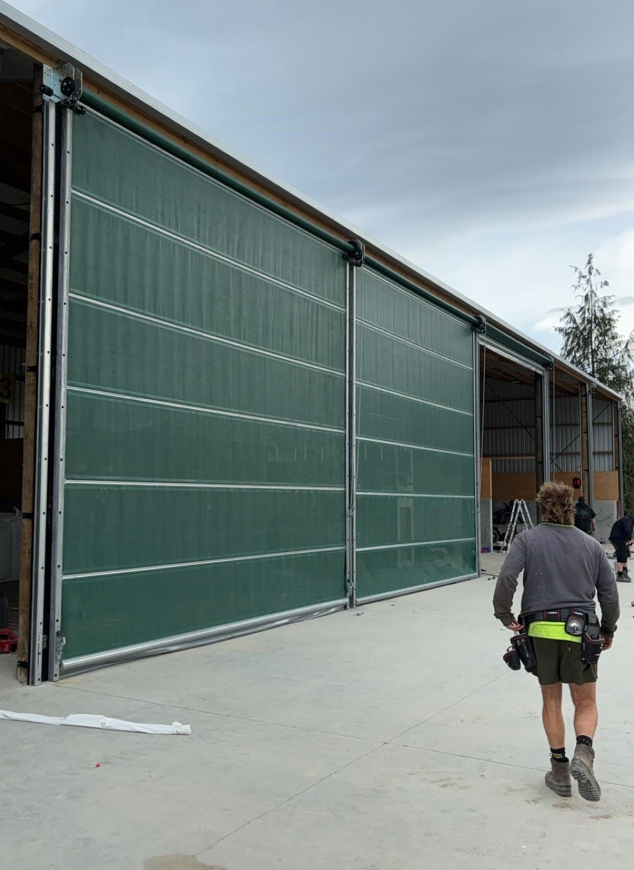 A man is walking in front of a large green building.