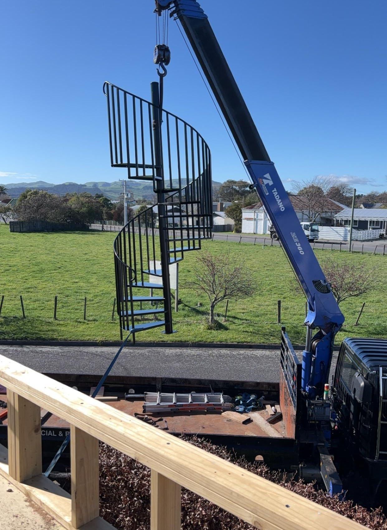 A crane is lifting a spiral staircase in a field.
