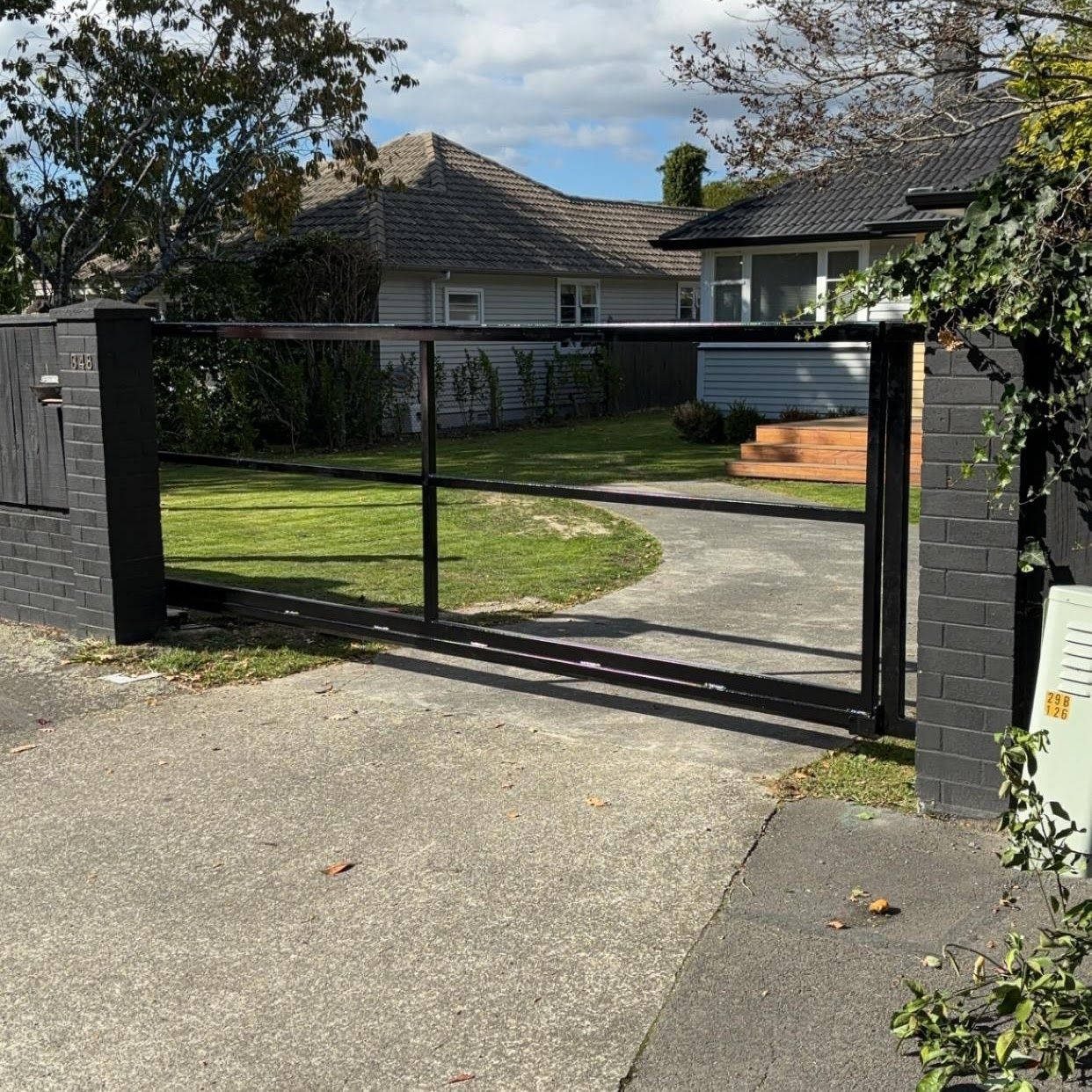 A sliding gate is open to a driveway in front of a house.