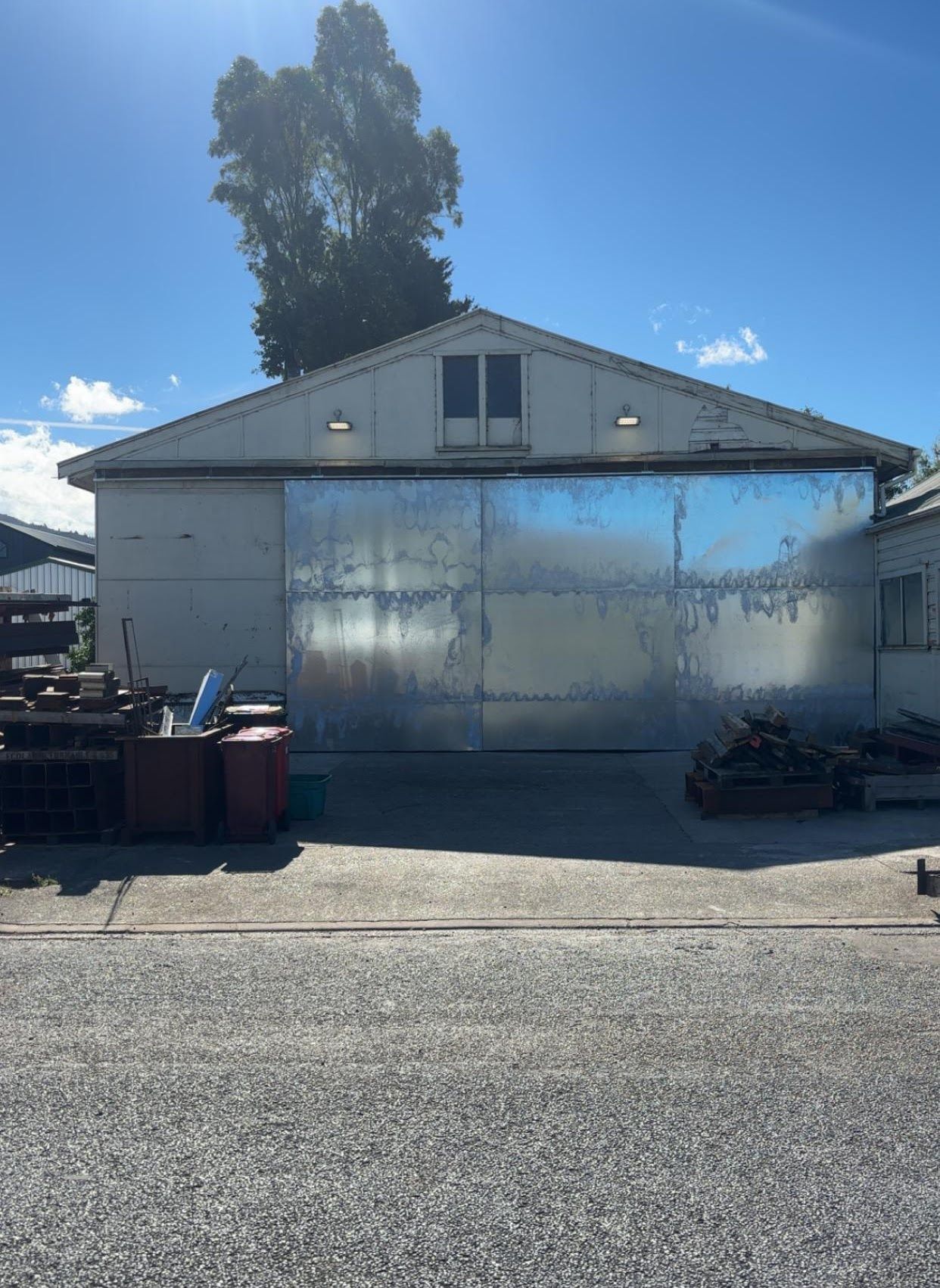 A large metal building with a sliding garage door is sitting on the side of the road.