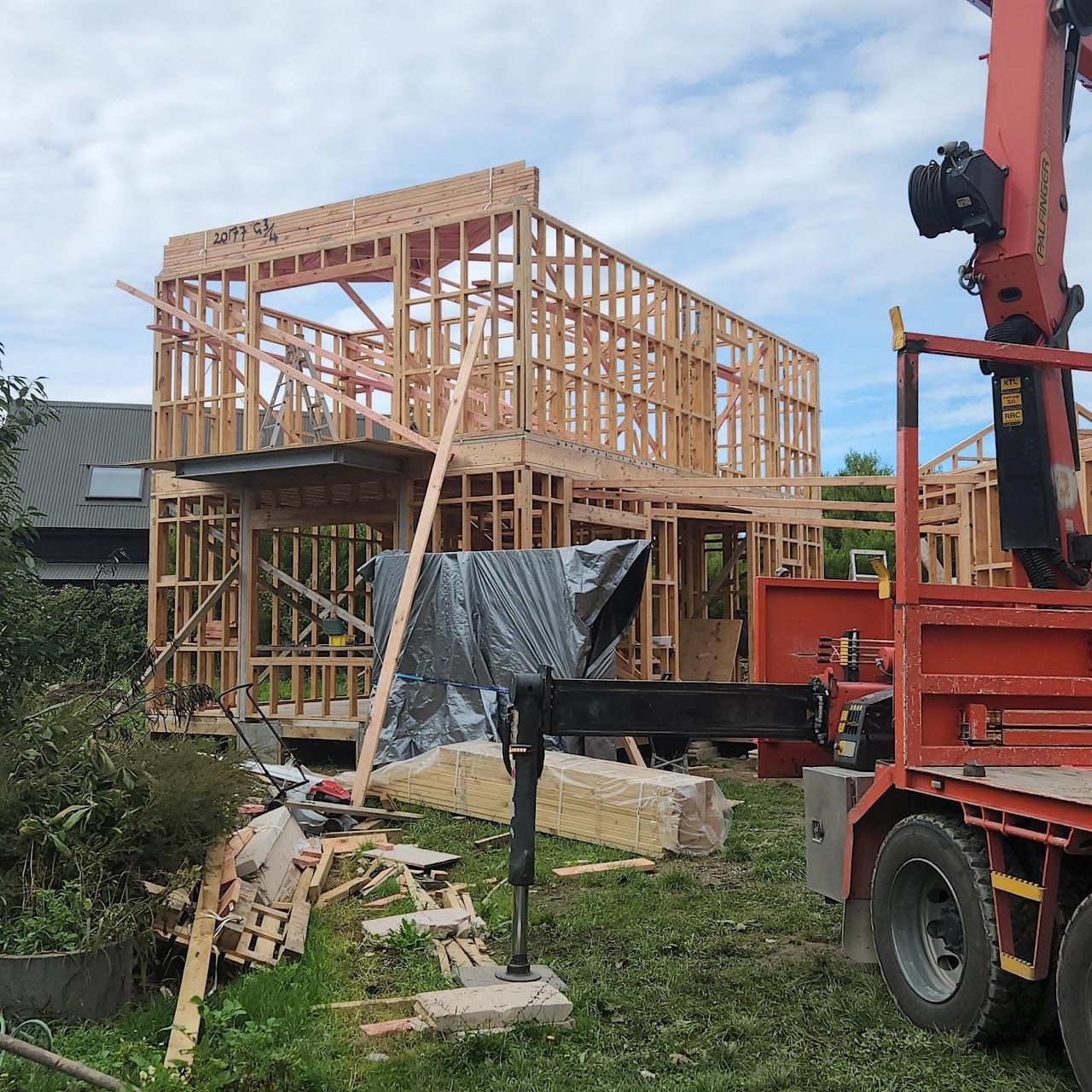 A red truck is parked in front of a house under construction.