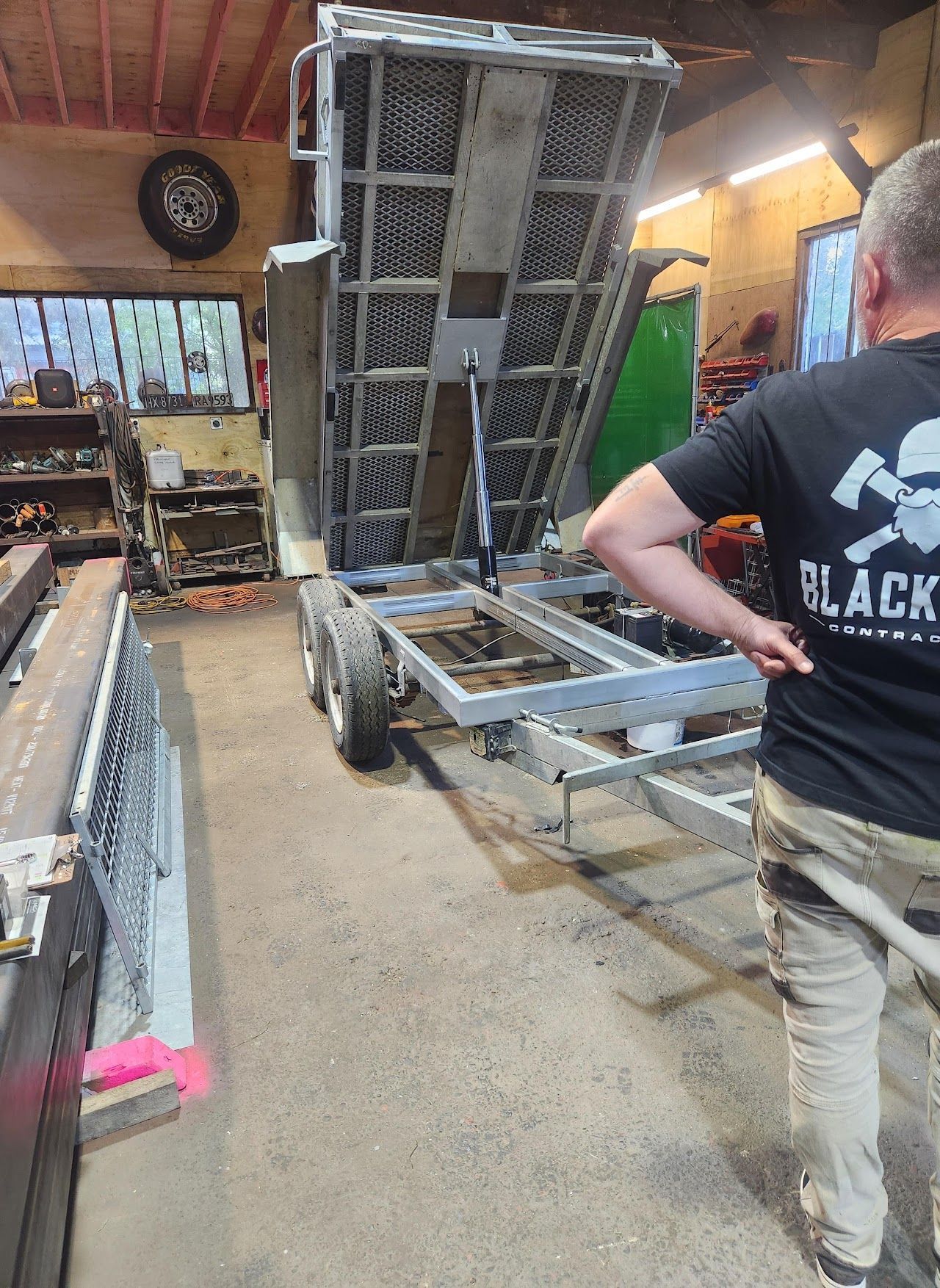 A man in a black shirt is standing in front of a trailer in a garage.
