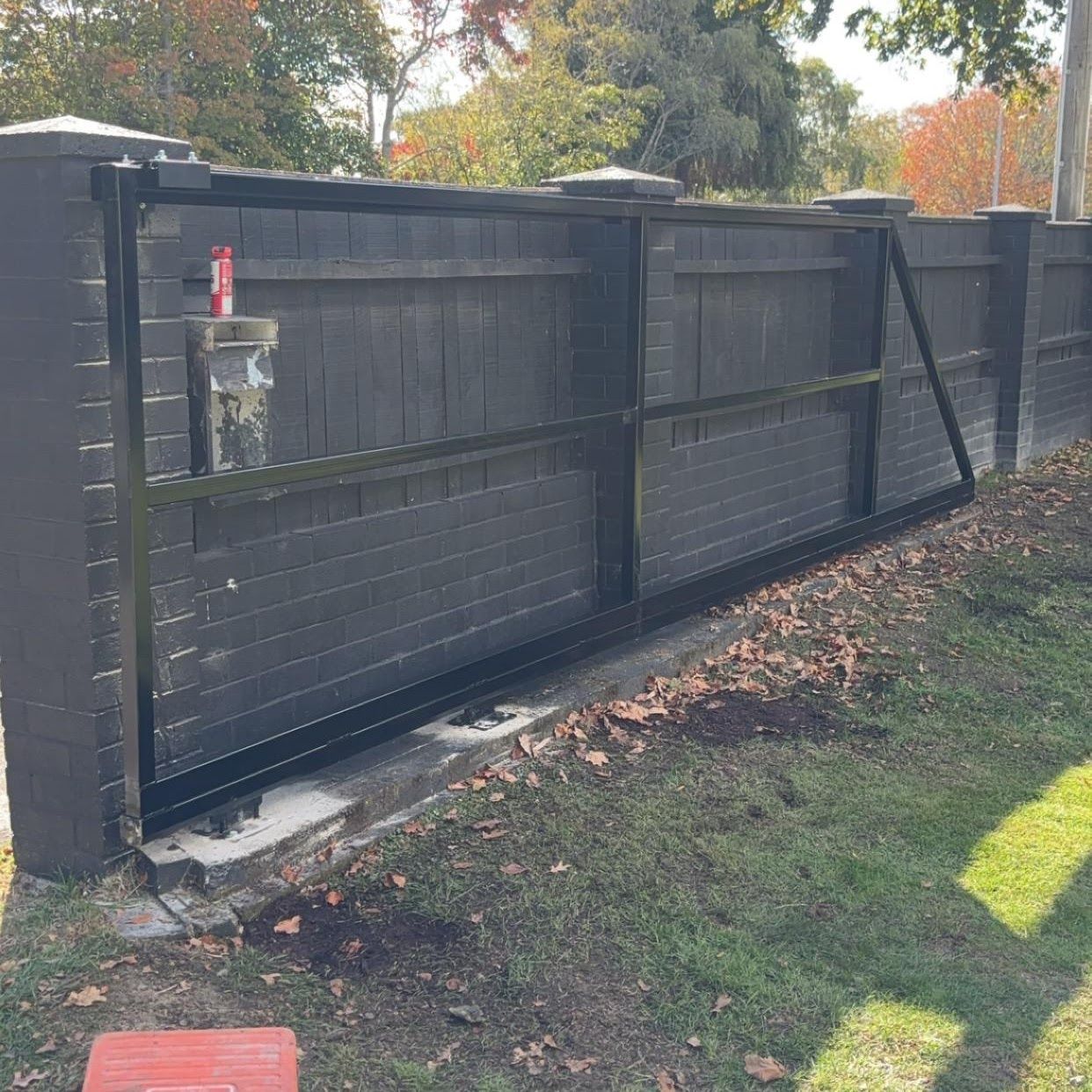 A sliding gate is sitting next to a brick fence.