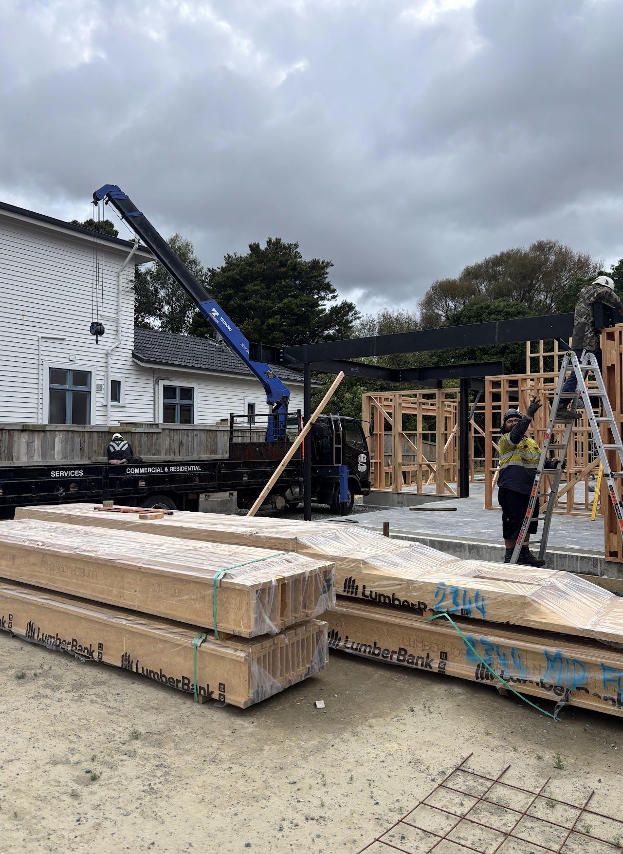 A crane is lifting a stack of wooden beams on a construction site.