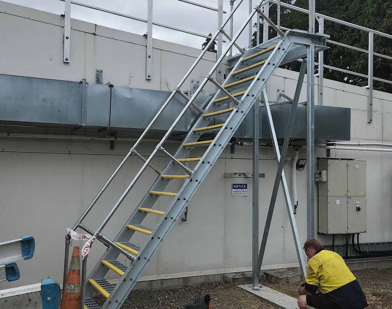 A man in a yellow shirt is kneeling next to a metal staircase.