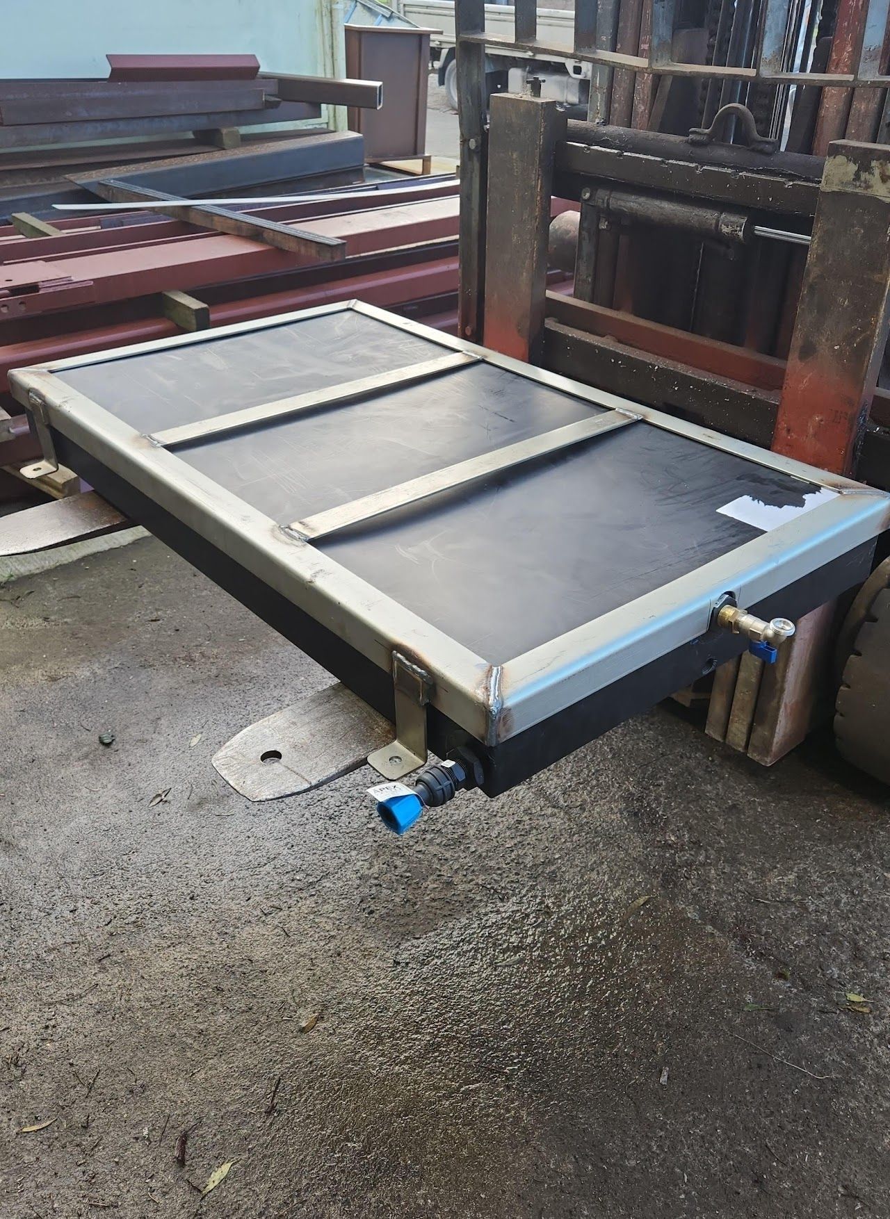 A large piece of metal is sitting on the ground next to a forklift.