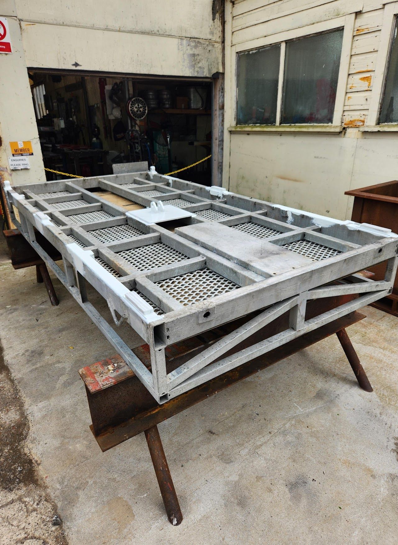A metal frame is sitting on top of a wooden table in front of a building.