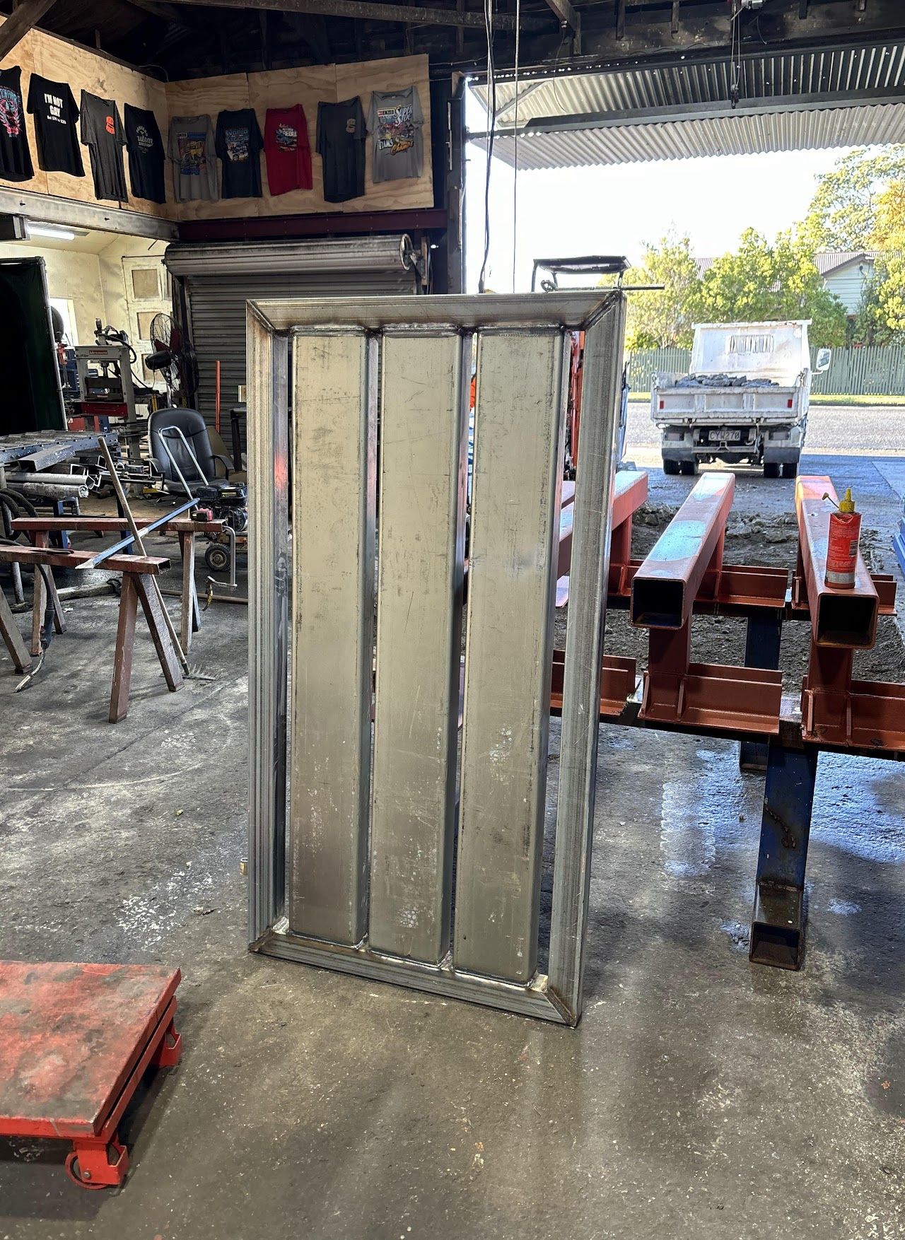 A metal door is sitting in a garage next to a red pallet.