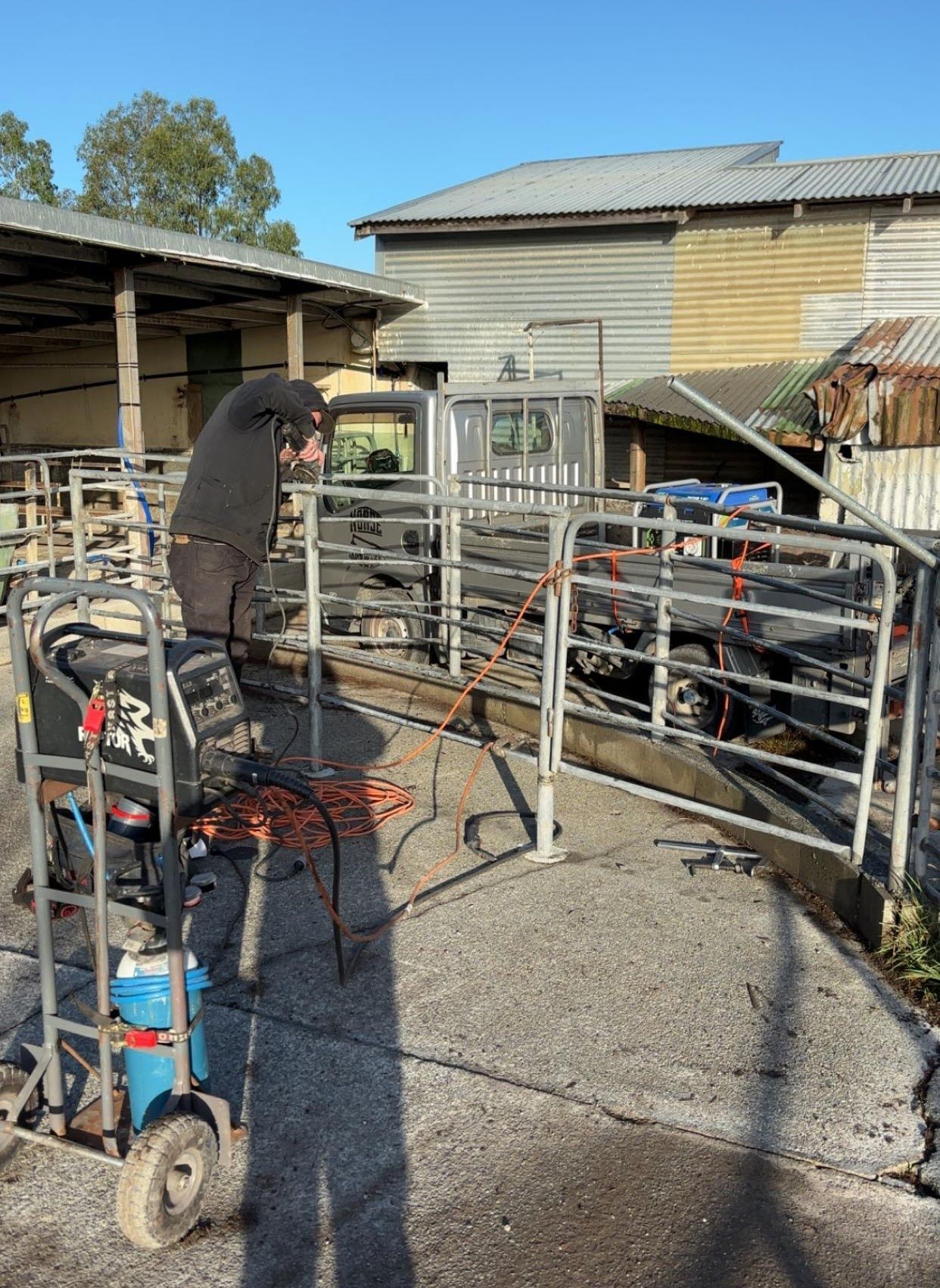 A man is welding a metal fence in a barn.