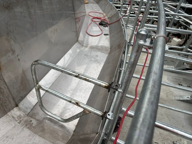 Inside view of a large metal basin with a metal handrail attached. Red wires and a metal frame are visible.