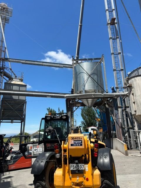 Yellow tractor in front of grain silos and metal infrastructure under a blue sky.