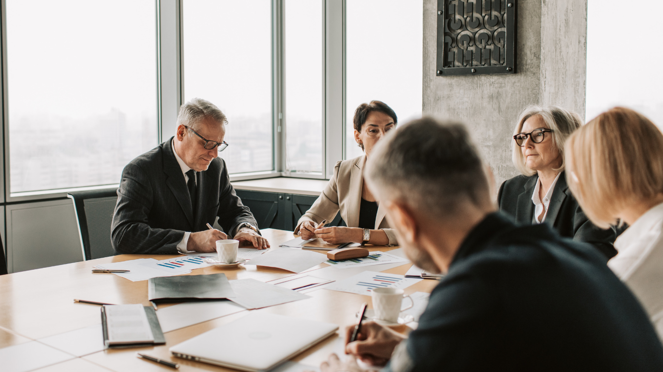 Businesspeople at a table reviewing papers in a brightly lit office.
