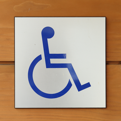 A blue, square-framed international symbol of access (wheelchair icon) on a white background mounted on wood.
