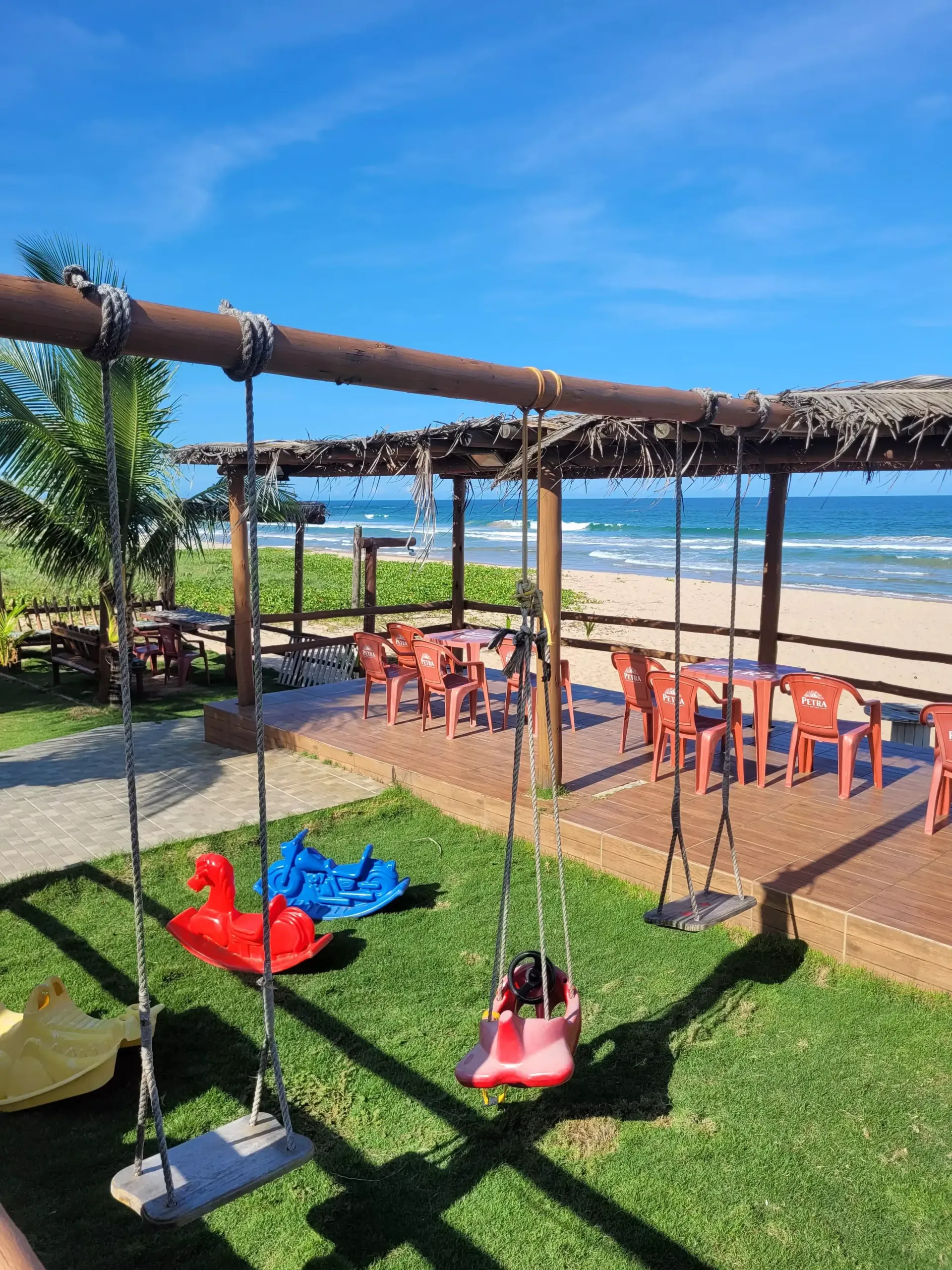 Um playground com balanços, mesas e cadeiras em frente à praia.-Pousada Águas de Piruí