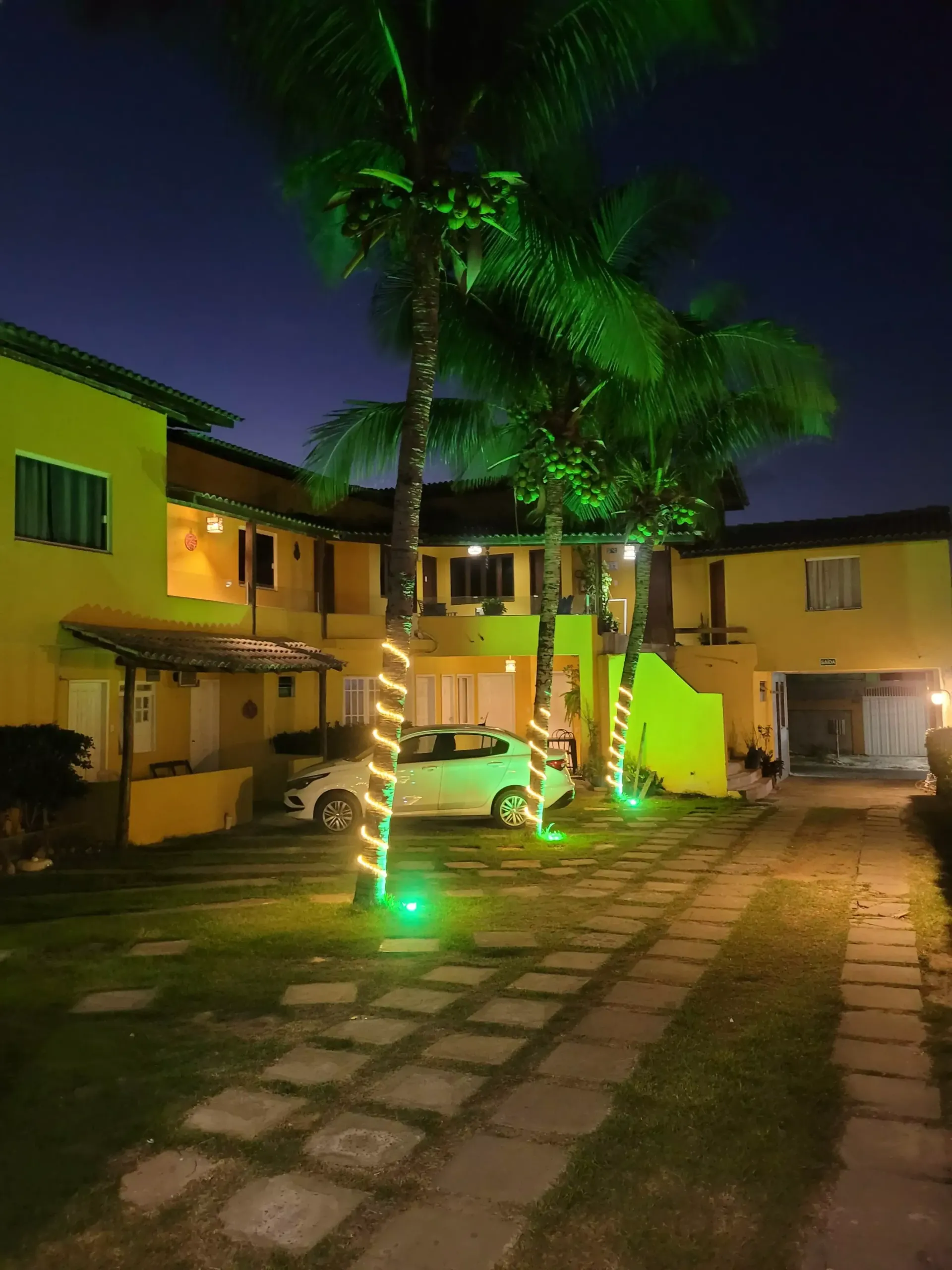 Um carro branco está estacionado em frente a um prédio amarelo à noite.-Pousada Águas de Piruí