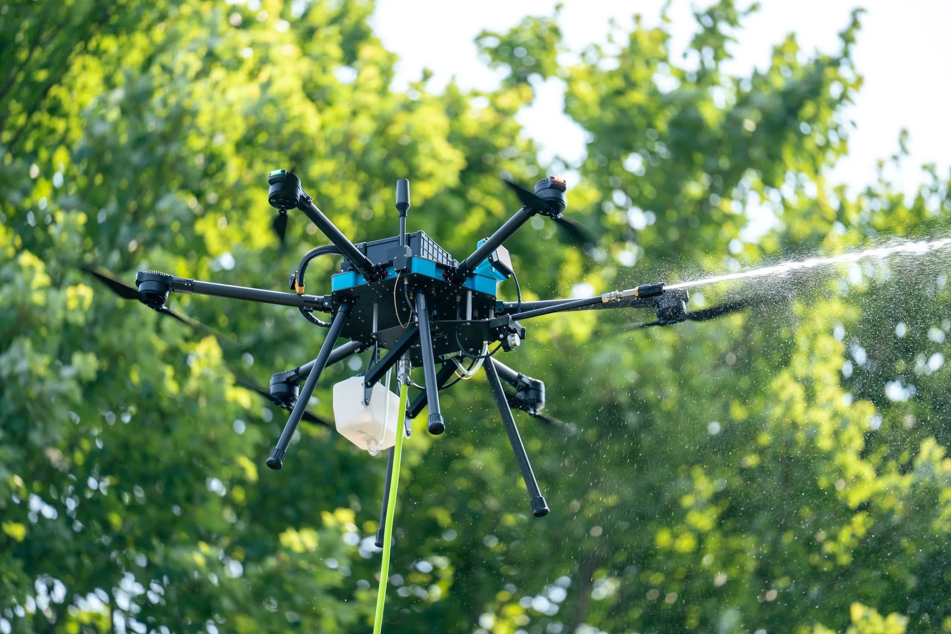 Agricultural drone spraying water over green trees outdoors