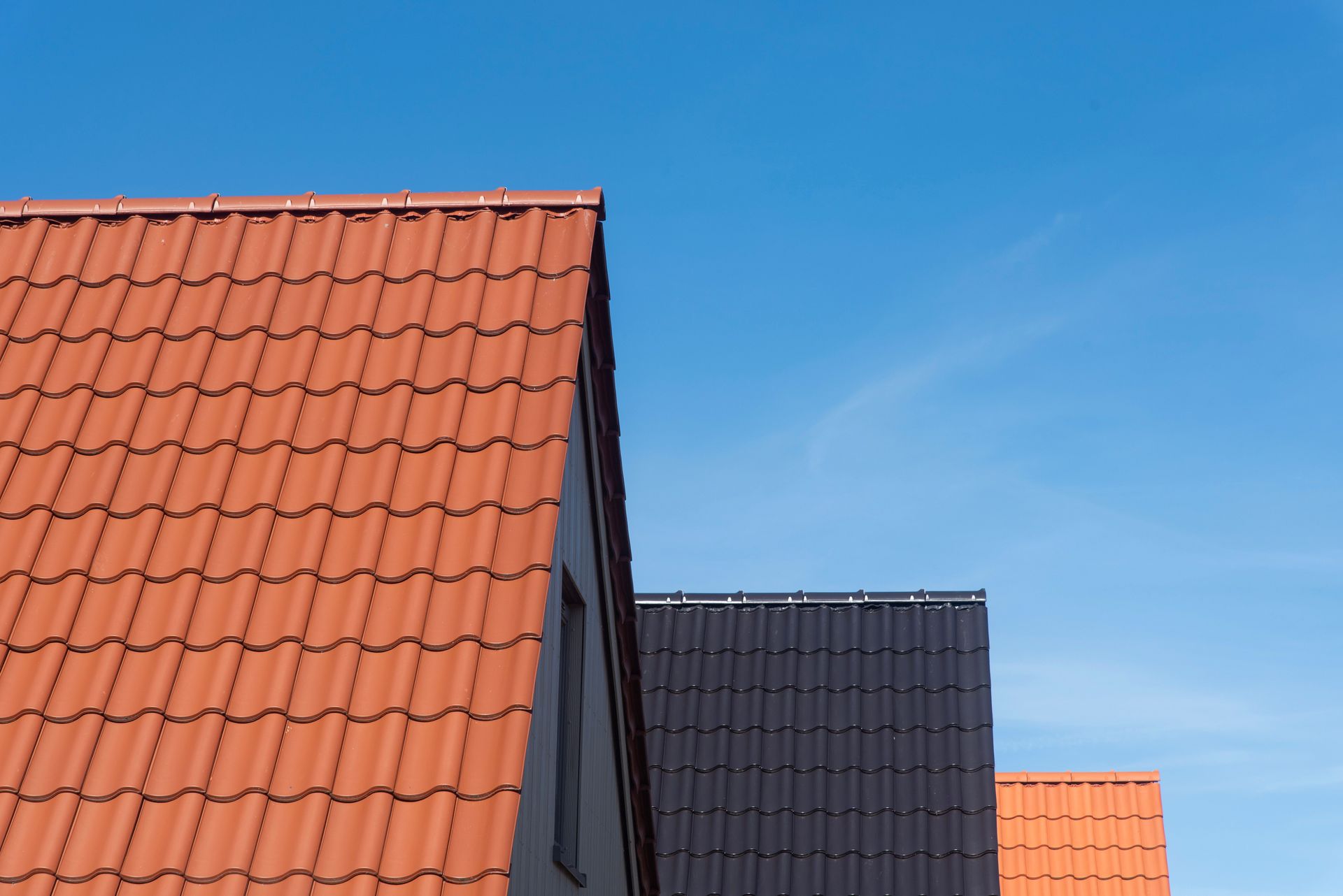 Rooftops with red, gray, and orange tiles beneath a clear blue sky.