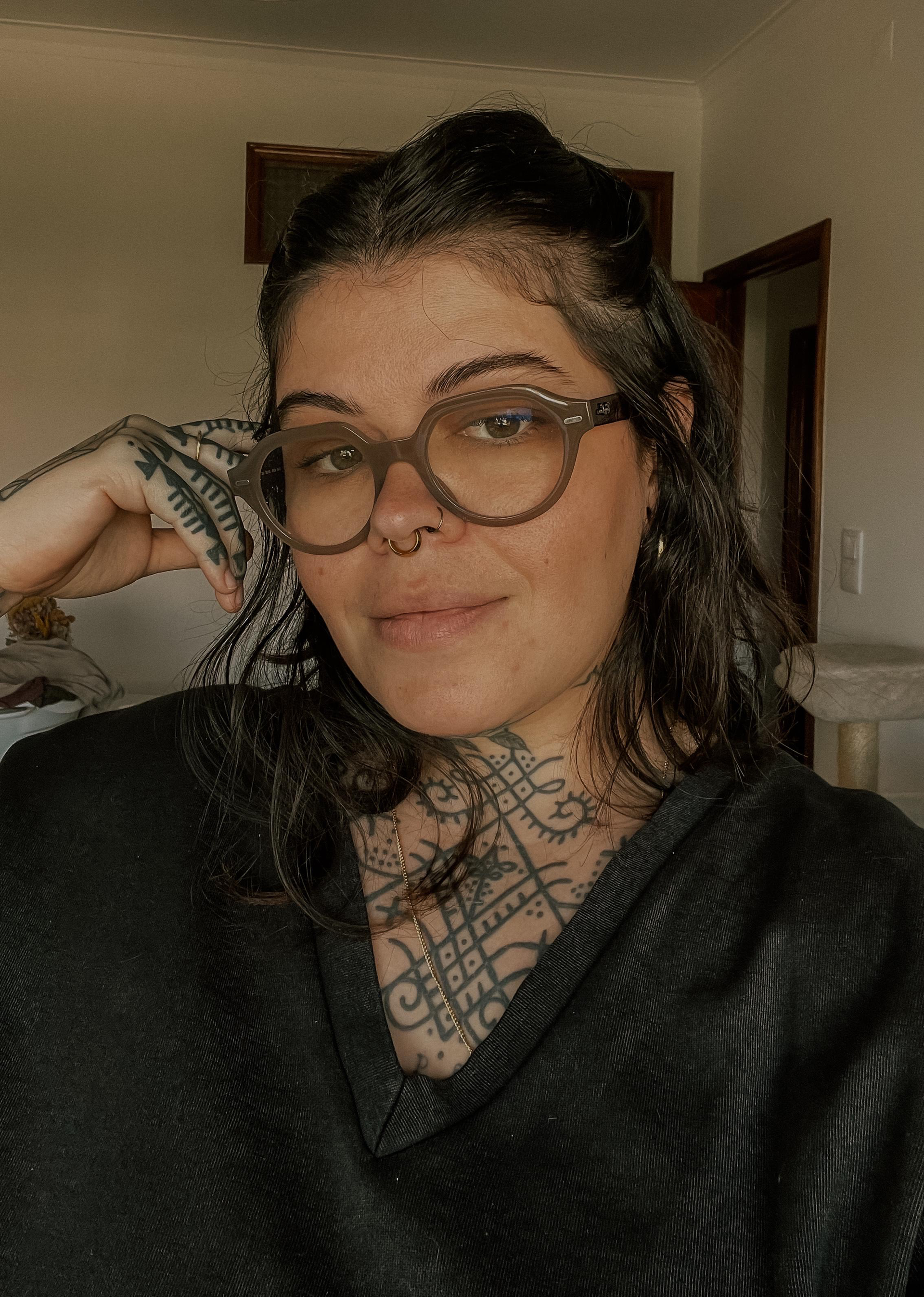 Uma mulher usando óculos e uma camisa preta tem uma tatuagem no peito.