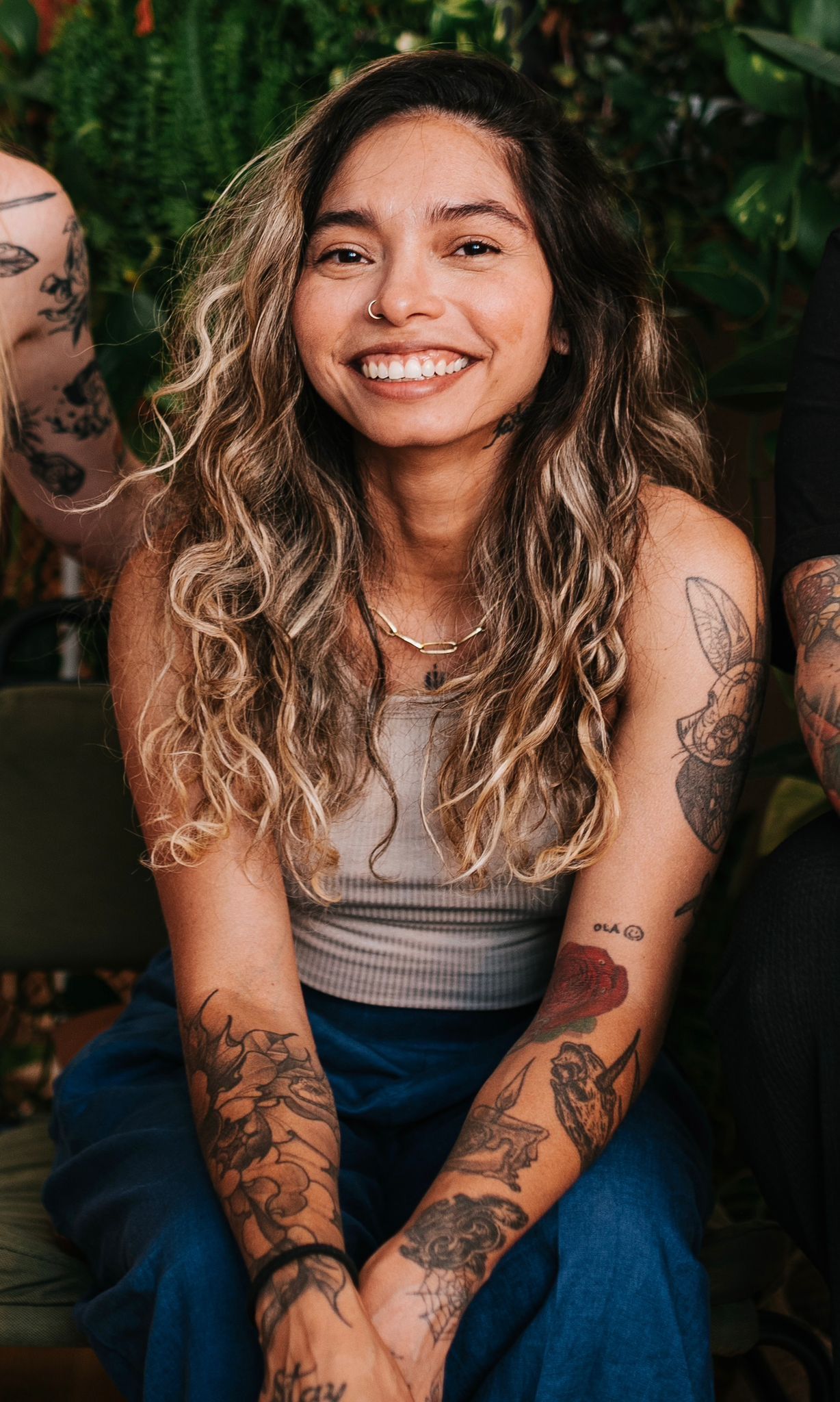 Uma mulher com tatuagens nos braços sorri sentada ao lado de um homem.