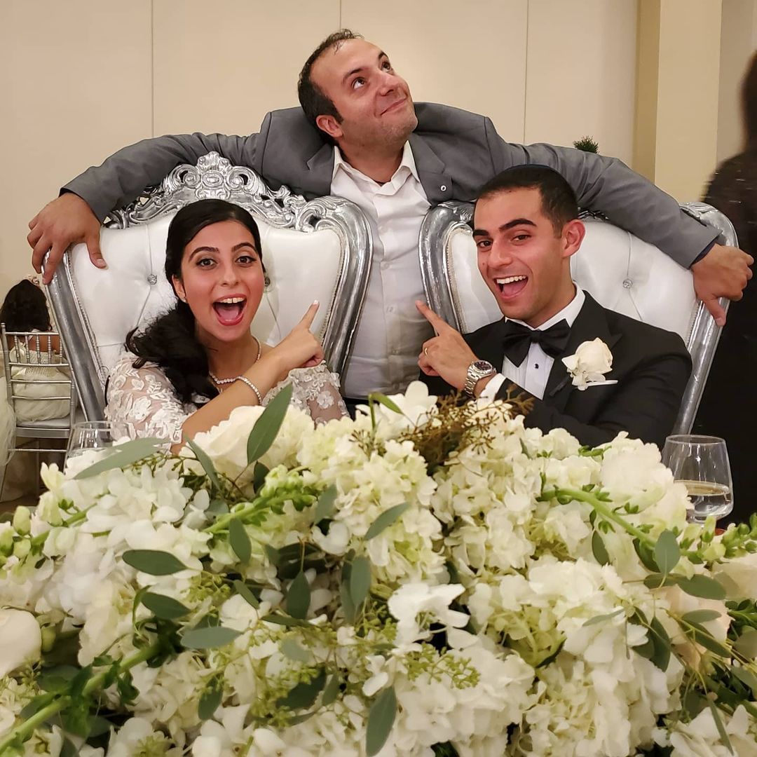 Wedding DJ Long Island, Bride and groom at wedding table with guest, all pointing up with excited expressions.