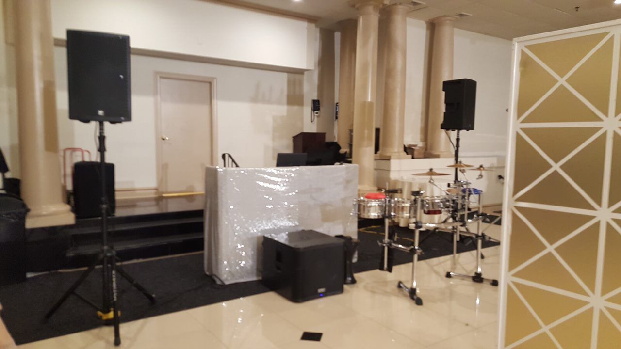 A stage setup with speakers, DJ equipment, and a drum kit in a room with columns.