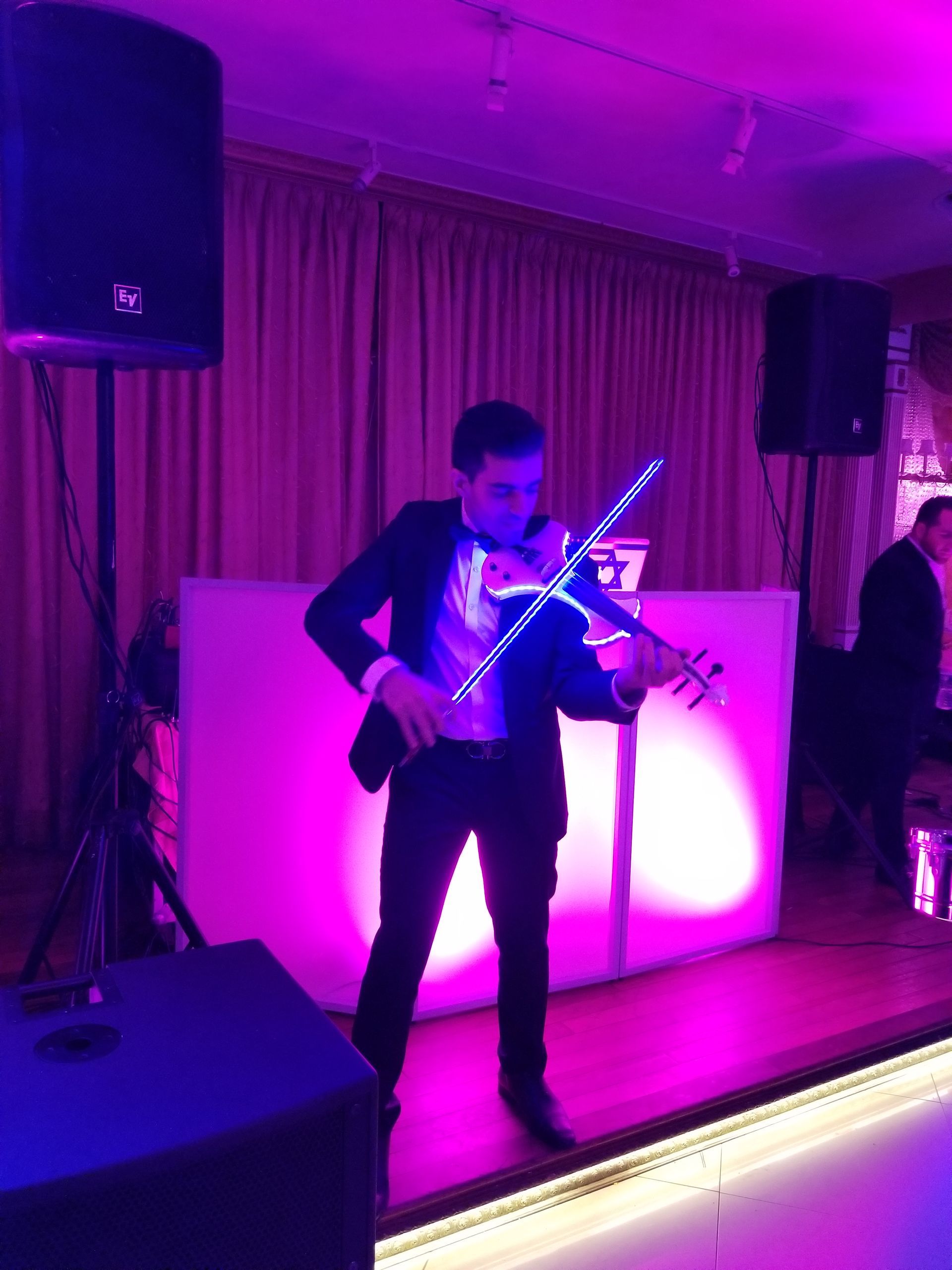 Man playing a glowing blue violin on stage, illuminated by pink and purple lights.