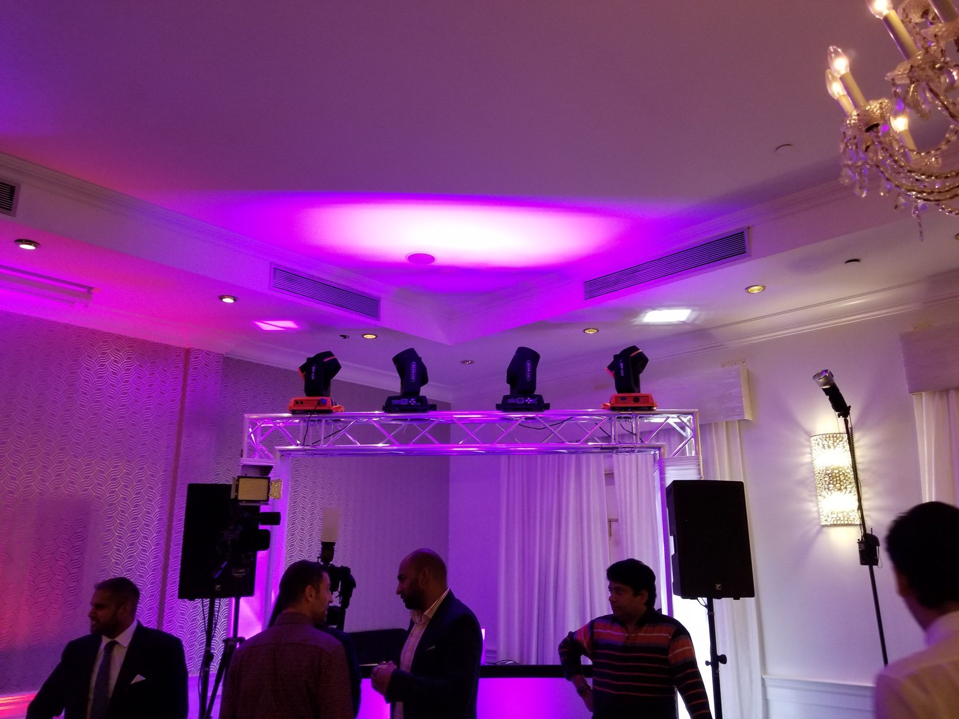 Event setup: Stage lighting, speakers, and people in a room with purple and white decor.