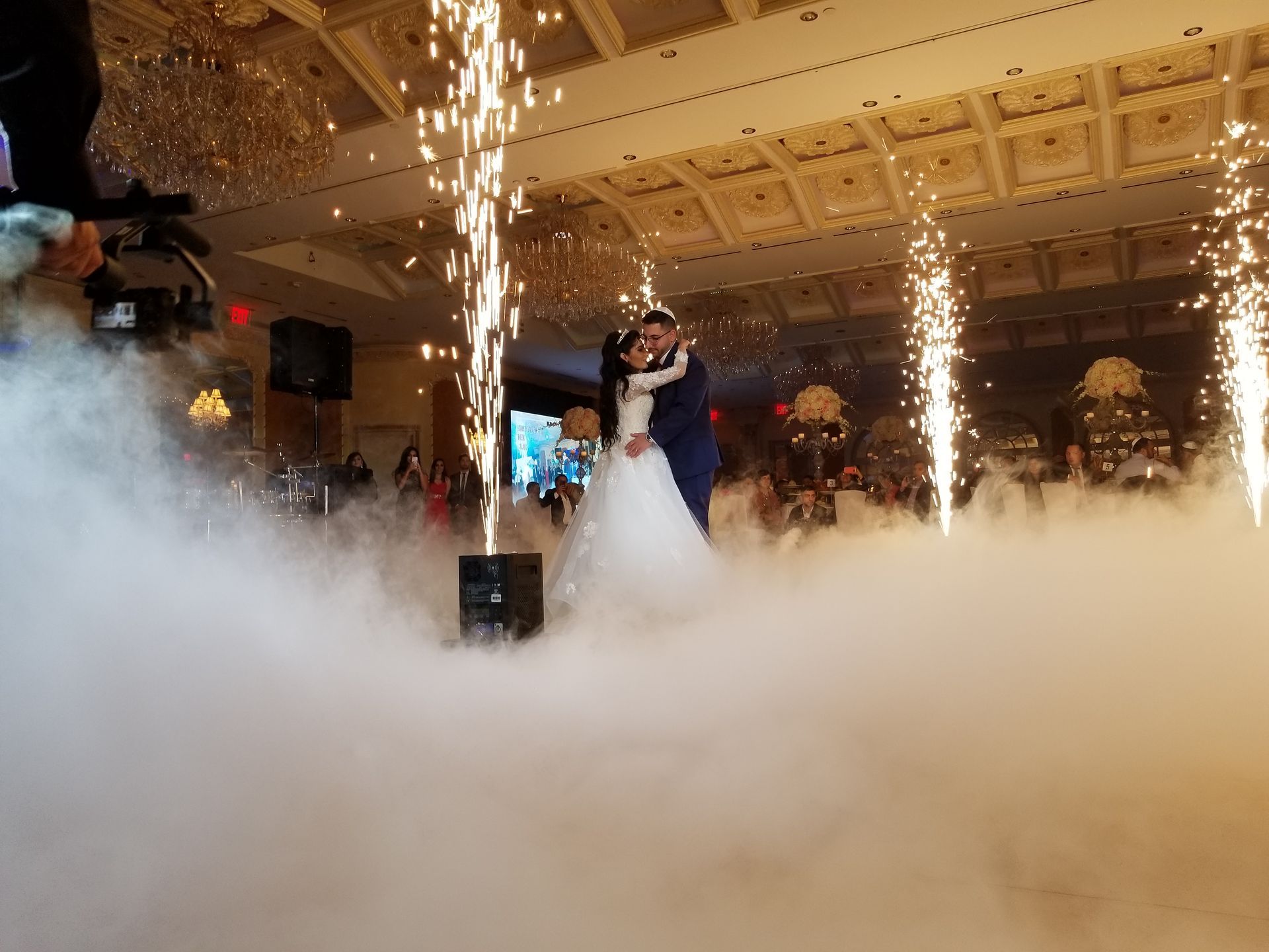 DJ stage setup lit with colorful lights.  Speakers, lights, and DJ equipment on a stage.  Elegant ballroom setting.